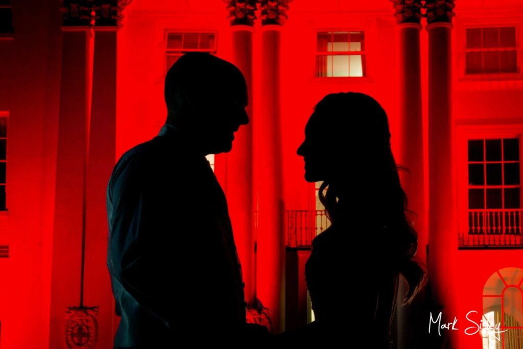The newlyweds in silhouette at the front of the floodlit red house