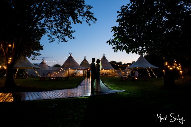 Dramatic pose of the newlyweds outside their floodlit tipi at dusk during their Dovecote Events summer wedding reception