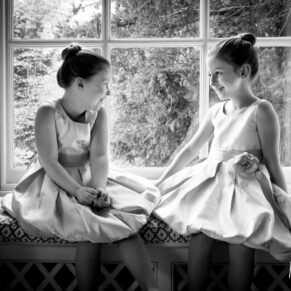 Black and white wedding photography in Buckinghamshire - window-lit image of young flower girls in window at Hartwell House Hotel