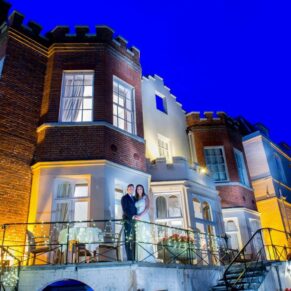 Bride and groom at dusk on the terrace of Taplow House Hotel on their wedding day with fairy lights in the railings