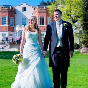 Bride and groom walking on the lawn in front of Taplow House hotel on their wedding day