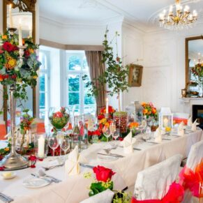 Autumnal wedding breakfast place setting with chestnuts, yellow and red berries, and orange and red roses in jars and ivy with bronze-sprayed eucalyptus branches