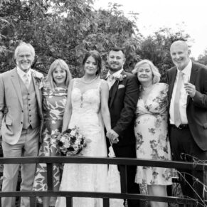 Photography of the newlyweds with their parents in a relaxed pose on the bridge  at their Sopwell House wedding
