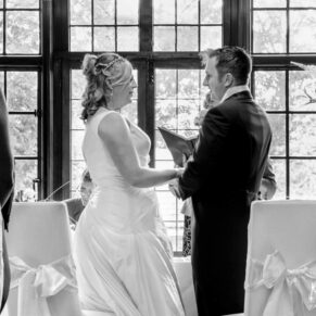 Photography of the indoor wedding civil ceremony in progress at the Bay Tree Hotel with a dramatic feature window framing the couple during their vows at their Burford venue