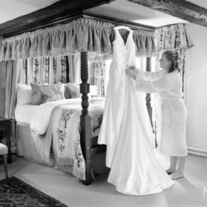 Photography of the wedding gown being tended to by the bride whilst it hangs from her four poster bed in the bridal suite at the Bay Tree Hotel in Burford