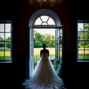 The bride in a lovely feature window captured from behind to showcase her gown with Bisham Abbey's distant views seen through the tall doorway