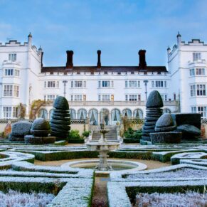 A stunning frosty blue sky wedding morning captured across the topiary towards the white fairy tale hotel exterior