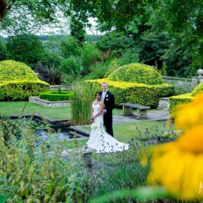 The bride and groom captured through the summer flowers in the Italian Garden at their Danesfield House wedding