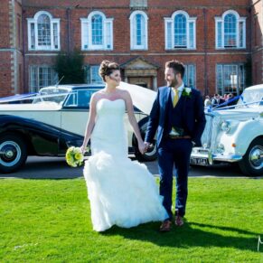 The newlyweds walking with their gorgeous cars in the background at their Dorton House wedding