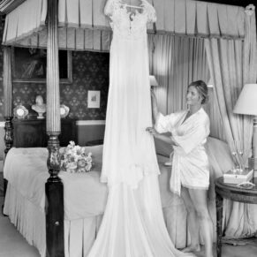 The bride adjusts her gown that's displayed on the four poster bed at her Hartwell House wedding 