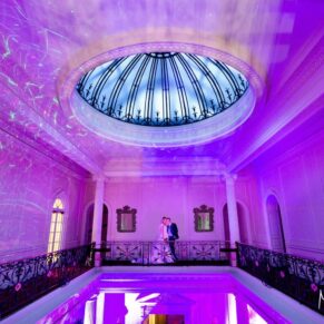 Classic and dramatic pose of the newlyweds on the balcony in the Great Hall lit with Hedsor House's bright and vibrant disco lighting