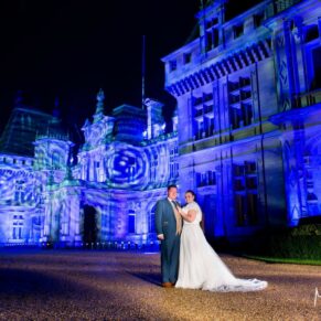Dramatic floodlit pose of the bride and groom in front of Waddesdon Manor after dark 