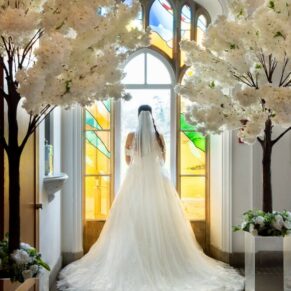 The back of the bride's dress captured in one of the many gorgeous stained glass windows at this Buckinghamshire venue 
