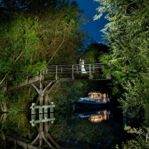 I do love a challenge, and shots don't get anymore adventurous than this on on the old bridge in the village of Hurley! Doing the walk through is one thing in bright daylight with the couple, doing again in pitch black conditions on the wedding day just elevates the challenge to another level. After a short drive from the Olde Bell Hotel at dusk, it's an 80 meter walk down a muddy and dark pathway to the river, thankfully I had an enthusiastic couple in wellies who were keen to realise my vision for this capture. Getting a couple, photographer, camera and lighting equipment to the location was one thing, but my shooting position was right beside the scarily deep lock! Miraculously we discovered on arrival that a gorgeous vintage boat had moored up perfectly just beyond the bridge, boy this shot was now coming together nicely. The logistics were now at the back of my mind, it was time to floodlight the magical vista in front of my camera (the only thing I could see at this stage was the interior lights on the boat)! I knew the second I looked at the back of camera that I'd nailed this shot in one take - it was now time to get us all back to the hotel - but boy I love this shot! The newlyweds on the old bridge across the River Thames at dusk captured on their Olde Bell Hotel wedding day in Hurley