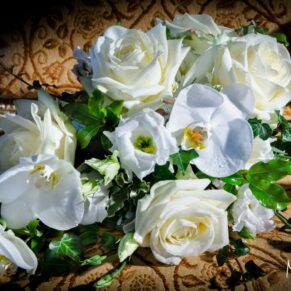 Beautiful bride's bouquet of white roses and orchids placed elegantly on an opulent gold fabric and illuminated with dramatic window lighting at Hedsor House  