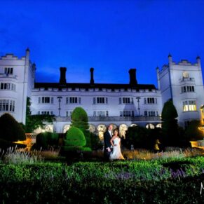 Atmospheric floodlighting has been used to illuminate the entire building for this dramatic pose with the newlyweds at their winter wedding at Danesfield House Hotel