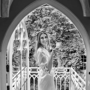 The bride in her silk dressing gown seen on the cottage balcony enjoying a glass of champagne before her church ceremony