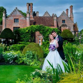 The newlyweds surrounded by gorgeous flower borders and architecture at their summer Chenies Manor wedding