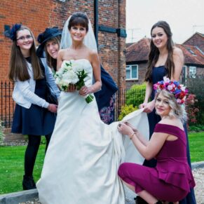 The ladies assist the bride with her gown in the grounds of the Kings Chapel in Old Amersham 