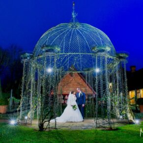 Buckinghamshire Winter Wedding Photography - the newlyweds framed by the floodlit rose arbour at The Dairy on the Waddesdon Estate 