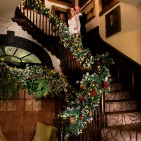 Buckinghamshire Winter Wedding Photography - the newlyweds pose on the Christmassy staircase at The Castle Hotel in Windsor