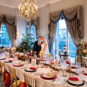 The couple pose beside their Christmas themed dining table in the Boudoir at their Cliveden House wedding  