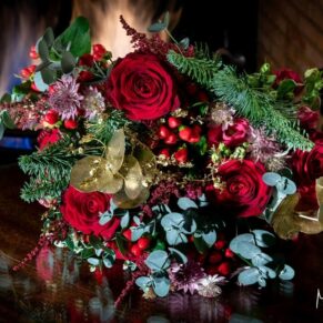 Stunning red Christmas wedding bouquet placed by the lit fireplace in the library at Cliveden House for a striking photography opportunity 