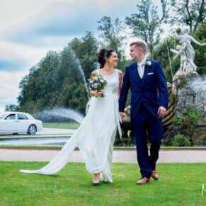 The couple walk towards to camera with the Fountain of Love behind them at their Cliveden House wedding reception