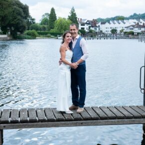 The bride and groom pose on the jetty for a lovely full length portrait beside the river in Marlow