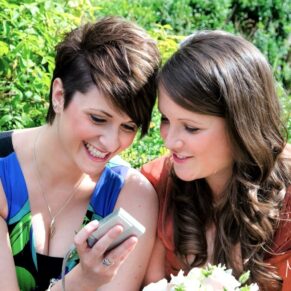 Two young ladies checking their phones during the wedding drinks reception at Danesfield House 