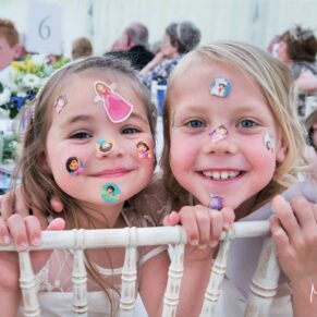 Two smiling flower girls covered in transfer stickers smile for the camera at this Dorton House marquee wedding in Buckinghamshire 