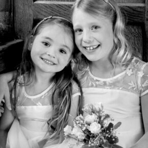 Two young smiling flower girls captured with dramatic window lighting inside this old oak panelled window at Dorton House