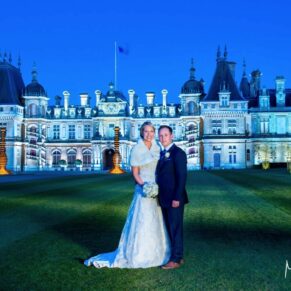 The newly married couple in front of the floodlit Waddesdon Manor at dusk with gorgeous dusky blue skies above 