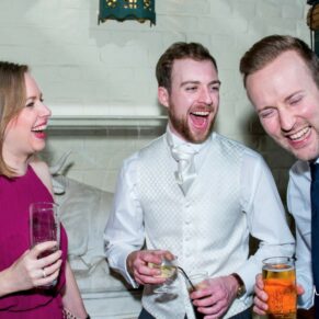 Reportage image of three giggling guests taken during the lively drinks reception in the Wintergarden at The Dairy on the Waddesdon Estate