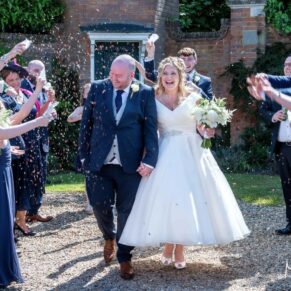 Fun confetti aisle moment in front of the clock tower at the Tudor Barn in Burnham