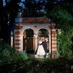 The newlyweds in a dramatic pose at dusk in the Tudor Barn's floodlit follyly
