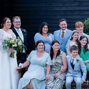 Relaxed family wedding pose with the bride and groom captured at the front of the barn on a summer's day at The Olde Bell in Hurley