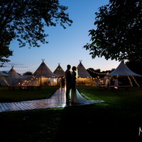 The newlyweds pose for the camera at night-time outside the illuminated tipi at dusk