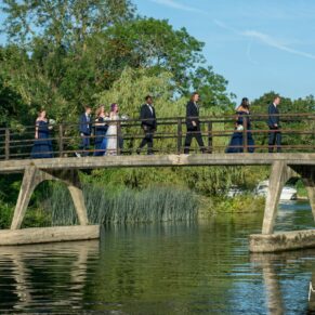 The newlyweds stroll over the bridge with their wedding bridal party on this glorious summers evening at The Great House in Sonning