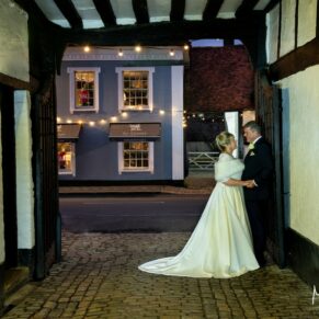 The bride and groom captured through the archway with views of Old Amersham High Street in the distance at their Kings Chapel wedding reception