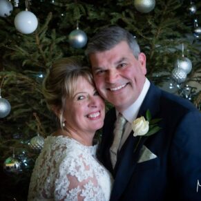 The newlyweds pose for a portrait beside the Christmas tree at their Kings Chapel wedding reception in Old Amersham 