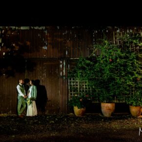 Artistic wedding photography at night-time of the newlyweds stood against their Buckinghamshire barn venue