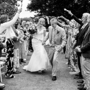 Black and white photography of bride and groom dashing through the confetti aisle at their Bisham Abbey Buckinghamshire wedding 