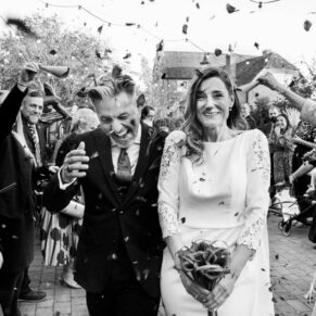 Confetti photography of the smiling bride and groom dashing between their guests at their Winters Tale Country Barn wedding in Buckinghamshire